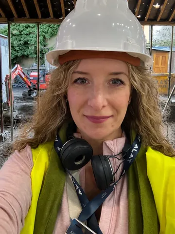 Jenny on demolition day, wearing a hard hat and hi-vis vest on site